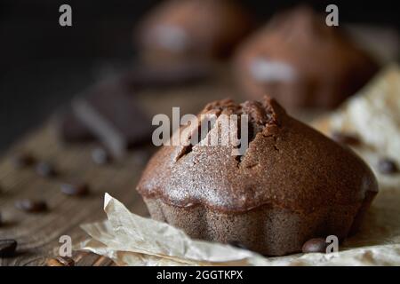 Muffins au chocolat faits maison sur parchemin avec grains de café et morceaux de chocolat. Arrière-plan en bois sombre, gros plan, mise au point sélective Banque D'Images