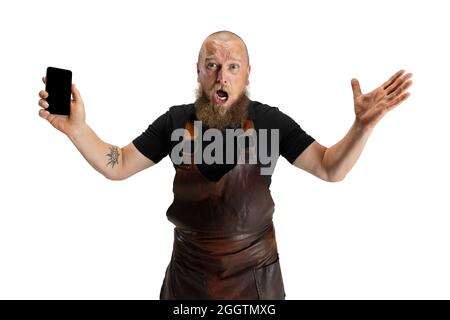 Portrait comique de chauve barbu musclé, forgeron en tablier de cuir ou uniforme isolé sur fond blanc de studio. Concept de travail, rétro Banque D'Images