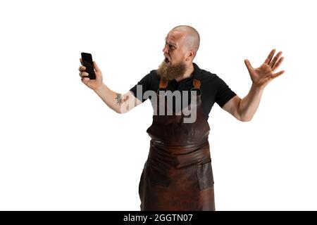 Portrait comique de chauve barbu musclé, forgeron en tablier de cuir ou uniforme isolé sur fond blanc de studio. Concept de travail, rétro Banque D'Images