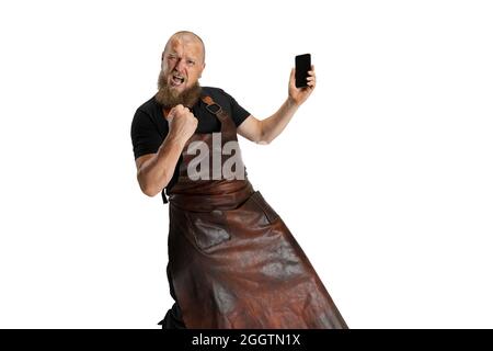 Portrait comique de chauve barbu musclé, forgeron en tablier de cuir ou uniforme isolé sur fond blanc de studio. Concept de travail, rétro Banque D'Images