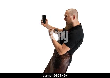 Portrait comique de chauve barbu musclé, forgeron en tablier de cuir ou uniforme isolé sur fond blanc de studio. Concept de travail, rétro Banque D'Images