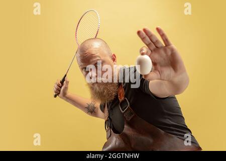 Portrait comique de chauve barbu musclé, forgeron en tablier de cuir ou uniforme isolé sur fond jaune de studio. Concept de travail, rétro Banque D'Images