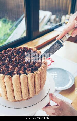 vue rapprochée des mains des femmes coupant le gâteau de tiramisu Banque D'Images