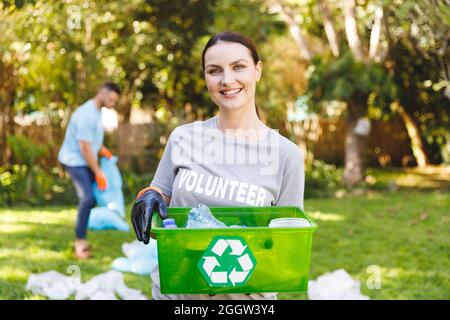 Portrait d'une femme caucasienne souriante tenant une boîte de recyclage, nettoyant la campagne avec son mari Banque D'Images