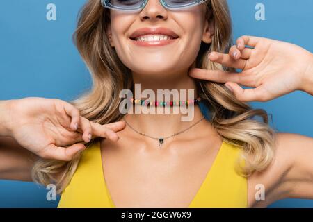courte vue de la jeune femme joyeuse dans un collier coloré orné de perles souriant isolé sur bleu Banque D'Images