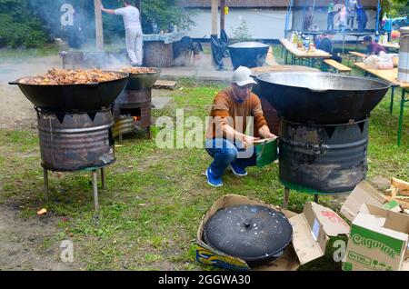 Chaudrons remplis de riz pilaf sur des poêles à bois mobiles. L'homme met un morceau de bois dans un des fourneaux. Célébration du Ramadan, rupture du jeûne. Ma Banque D'Images
