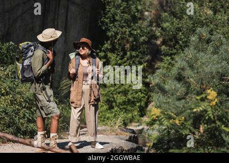 Couple multiethnique avec sacs à dos debout dans la forêt Banque D'Images