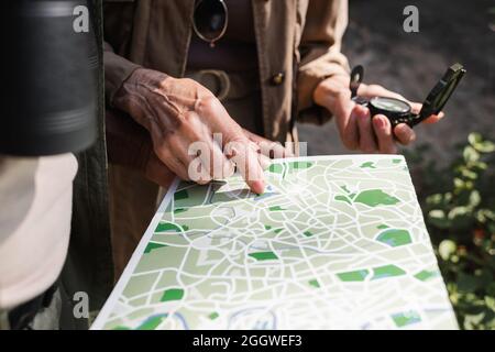 Vue rognée d'une femme âgée avec boussole pointant sur la carte près du mari afro-américain Banque D'Images