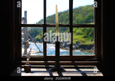 Bougie blanche dans un ancien porte-bougie, sur un vieux bureau, à côté d'un stylo à douille dans un puits d'encre, en face d'une fenêtre, donnant sur la mer. Banque D'Images