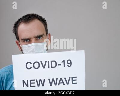 Un homme de nationalité caucasienne dans un masque médical sur le fond d'une notice avec l'inscription: Covid -19 nouvelle vague. Le concept de lutte contre le Banque D'Images