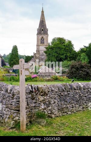 Une vue lointaine de l'église à Parwich avec un panneau de chemin de pied et un mur de pierre au premier plan. Banque D'Images