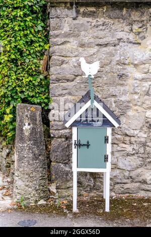 Un porte-oeufs dans le style d'un chalet suisse avec du coq sur le dessus annonçant des oeufs à vendre pendus contre un mur de pierre. Banque D'Images