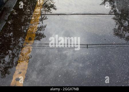 Reflet de l'ombre du câble électrique, du ciel et de l'arbre sur la route après la pluie Banque D'Images