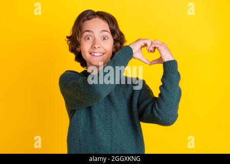 Portrait d'un joli gars gai émerveillé montrant la forme du coeur isolé sur fond jaune vif Banque D'Images