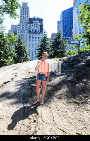 Jeune femme debout sur quelques rochers à Central Park devant les bâtiments de New York. Banque D'Images