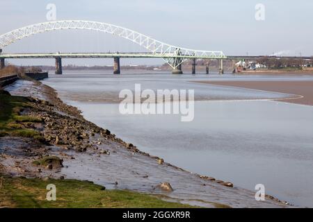 Le Mersey Tidal Bore approche du parc communautaire de Wigg Island à Runcorn avec le pont Silver Jubilee en arrière-plan Banque D'Images