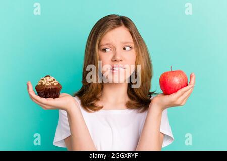 Photo portrait fille mise à l'échelle doux cupcake pomme mordant lèvre incertain obtenu doute isolé couleur sarcelle fond Banque D'Images