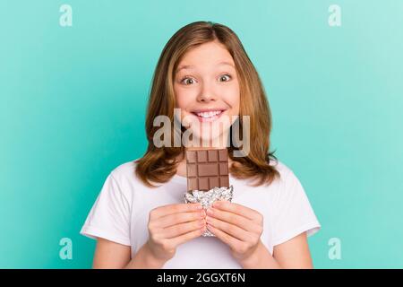 Photo portrait fille sourire heureux manger chocolat isolé couleur teal vif fond Banque D'Images