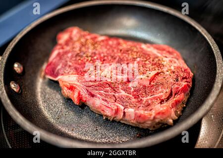 Macro-gros plan de la côte de ribeye non cuite à l'herbe non cuite, viande de bœuf aux yeux cuisson sur une poêle à frire antiadhésive avec assaisonnement au sel de poivre Banque D'Images