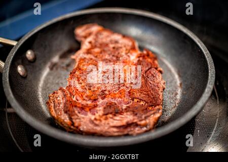 Gros plan de la croûte sur les côtes de ribeye rouges, alimentées en herbe, viande de bœuf cuisson sur une poêle à frire antiadhésive avec assaisonnement au sel de poivre Banque D'Images