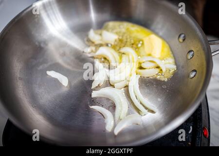 Macro gros plan d'une poêle en acier inoxydable avec de l'huile d'olive sauté et des tranches d'oignon doux blanc sur une cuisinière électrique dans la cuisine maison Banque D'Images