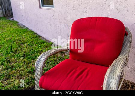 Gros plan d'un fauteuil d'extérieur en osier extérieur avec coussin rouge à la cour avant ou à l'arrière-cour avec pelouse en herbe verte au coucher du soleil à Naples, en Floride Banque D'Images