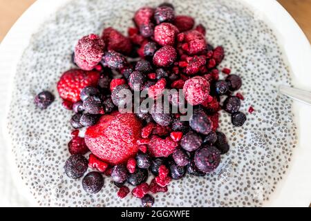 Gros plan plat macro de fraises fraîches crues, bleuets et framboises en graines de chia boudin au lait d'amande à la noix de cajou végétalienne avec cuillère Banque D'Images