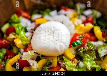 Macro-gros plan de salade romaine fraîche avec concombres, poivrons jaunes doux, tomates et fromage italien burrata mozzarella dans une assiette en bois Banque D'Images