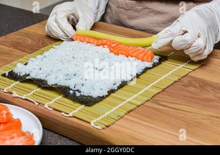 Processus de préparation des sushis.Les mains des femmes dans des gants en caoutchouc enveloppent des rouleaux pour les sushis, les sushis à la maison Banque D'Images