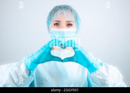 une infirmière dans une robe et un masque médicaux fait un geste sincère avec ses doigts Banque D'Images