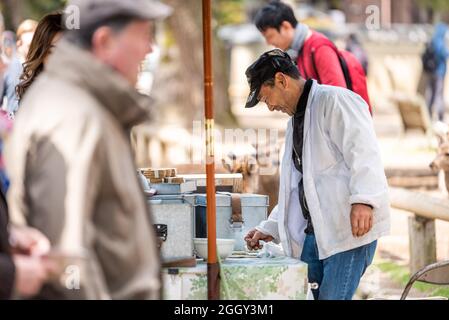 Nara, Japon - 14 avril 2019: Gens homme vendeur vendant des craquelins de riz aux touristes dans le parc de la ville pour nourrir les cerfs Banque D'Images