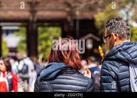 Nara, Japon - 14 avril 2019: Touristes candid personnes couple de retour à proximité au temple de Todaiji dans la ville pendant la journée par la porte mangeant dango mochi Banque D'Images