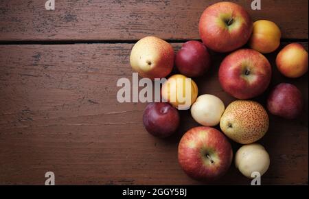 Fruits d'automne sur une table en bois. Pommes, poires, prunes, abricots sur fond rouge foncé. Placer pour le texte. Différents fruits sur bois texturé Banque D'Images