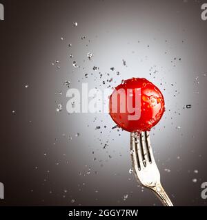 cerise de tomate sur une fourchette dans des éclaboussures d'eau. Arrière-plan noir et blanc Banque D'Images