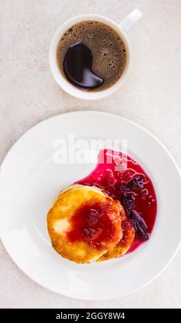 Gâteaux au fromage frais avec confiture de prune et une tasse avec café fraîchement préparé sur une table légère, vue du dessus. Réveillez-vous le matin, commencez une nouvelle journée. Hé Banque D'Images