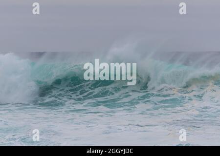 Une couleur vert turquoise en colère boucle massive d'une vague alors qu'il roule des barils le long de l'océan. La brume blanche et la mousse de la vague sont mousseuse Banque D'Images