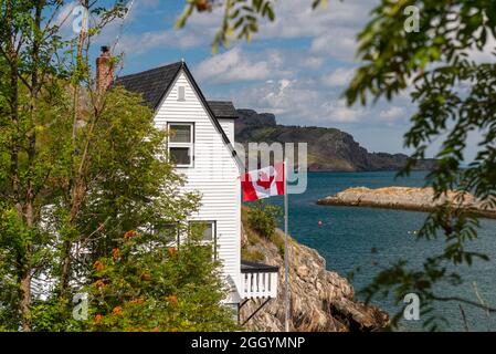 Un toit en bois noir au coin d'un cottage en bois blanc. Le bâtiment est au bord d'une falaise. Il y a un drapeau canadien sur la terrasse. Banque D'Images