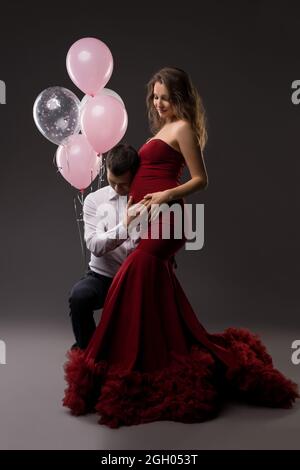 Jeune couple enceinte souriant touchant le ventre sur fond gris Banque D'Images