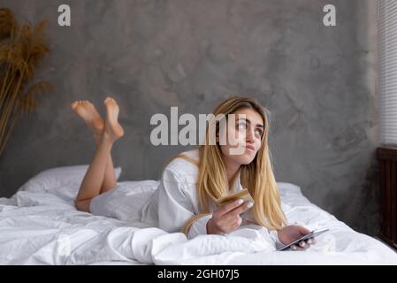 Portrait d'une jeune belle fille caucasienne couché sur le lit à la maison, shopping en ligne. . Banque D'Images