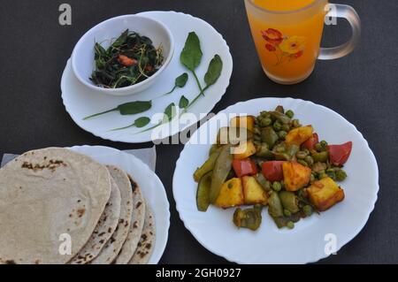 Photo de matar paneer mix légumes, saag (verts) et rôti (pain indien) sur des assiettes blanches et jus sur une table noire Banque D'Images