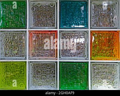 Une fenêtre colorée en vitraux. Rangées de carrés de verre dans des tons de bleu, rouge, jaune et verdâtre avec une surface texturée et des reflets Banque D'Images