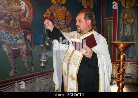 Un prêtre orthodoxe lit et chante des prières et fume avec une lampe pendant le baptême. Banque D'Images