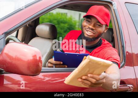 un travailleur de livraison africain assis dans une voiture et remettant un colis à quelqu'un Banque D'Images