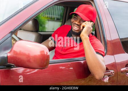 un travailleur de livraison africain qui fait un téléphone qui lui colle la tête hors de la voiture pour tenter de localiser un client Banque D'Images