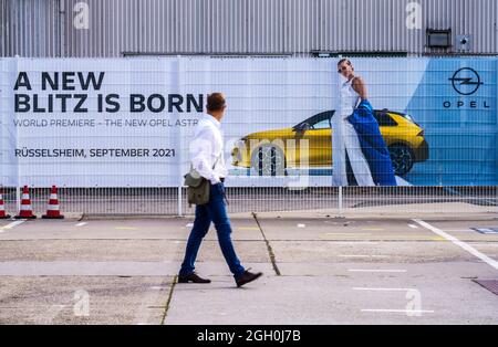 01 septembre 2021, Hessen, Rüsselsheim: Un homme passe devant une bannière publicitaire de la nouvelle Opel Astra. Le constructeur automobile Opel présente sa sixième génération de la nouvelle Opel Astra. La génération actuelle est également disponible sous forme de plug-in hybride et devrait être livrée à partir du début de 2022. Photo: Andreas Arnold/dpa Banque D'Images