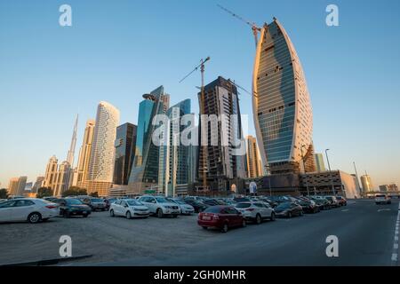 Voitures garées dans un terrain de terre, près de nouveaux gratte-ciels et de chantiers de construction. À Dubaï, Émirats arabes Unis. Banque D'Images