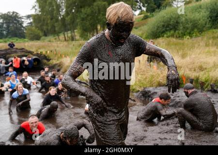 Les concurrents glissent et glissent dans la boue lors d'un événement Tough Mudder aux jardins du château de Cholmondeley à Malpas, Cheshire. Date de la photo: Samedi 4 septembre 2021. Banque D'Images