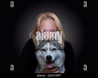 Portrait d'une fille et d'un chien avec des yeux bleus sur un fond sombre Banque D'Images