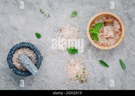 Sel rose de l'Himalaya dans le bol en bois avec la menthe poivrée ,sage,le thym, le basilic et l'origan sur fond de pierre. Sel de l'himalaya utilisé pour la cuisson et pour Banque D'Images