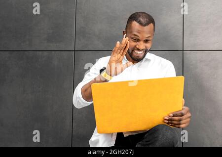 Un homme souriant se contente d'utiliser un ordinateur portable, d'avoir une conférence en ligne avec ses collègues. Un jeune homme d'affaires ou un étudiant élégant s'est fait un bonjour Banque D'Images